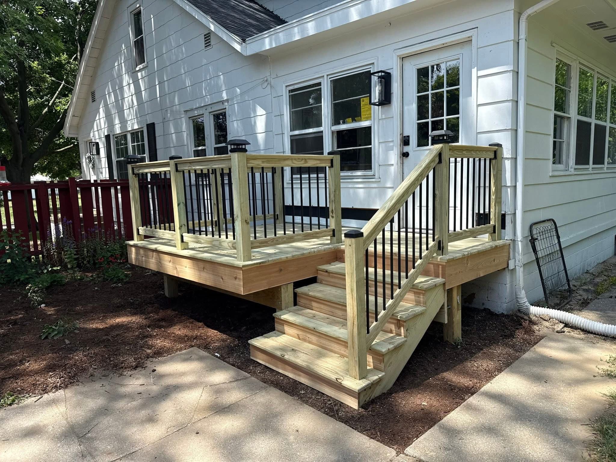 Newly built wooden deck with black metal railings and stairs on a white house.