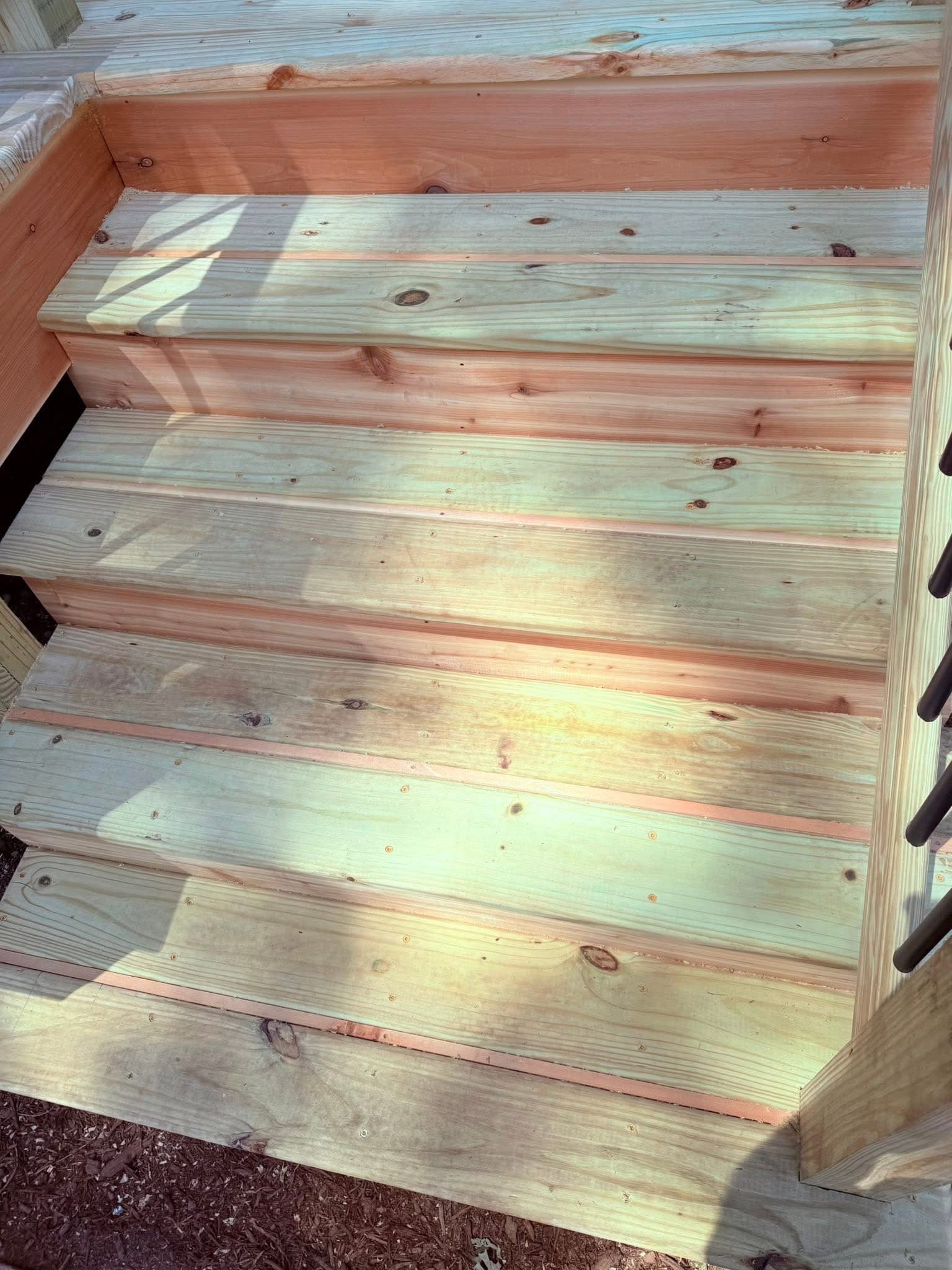 Newly built light-colored wooden deck stairs with natural knots and grain in sunlight.