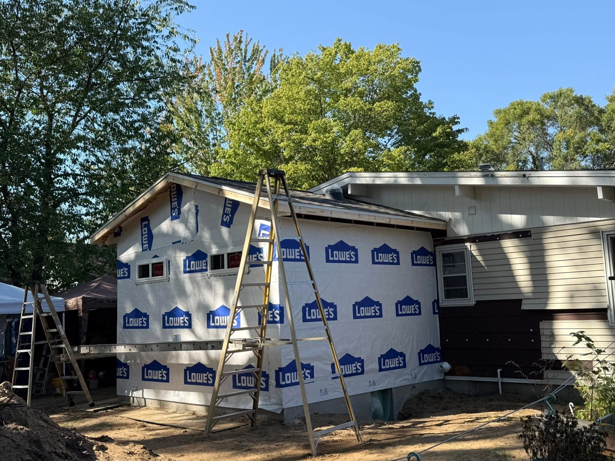 A house addition wrapped in Lowe's house wrap with ladders and scaffolding during construction.