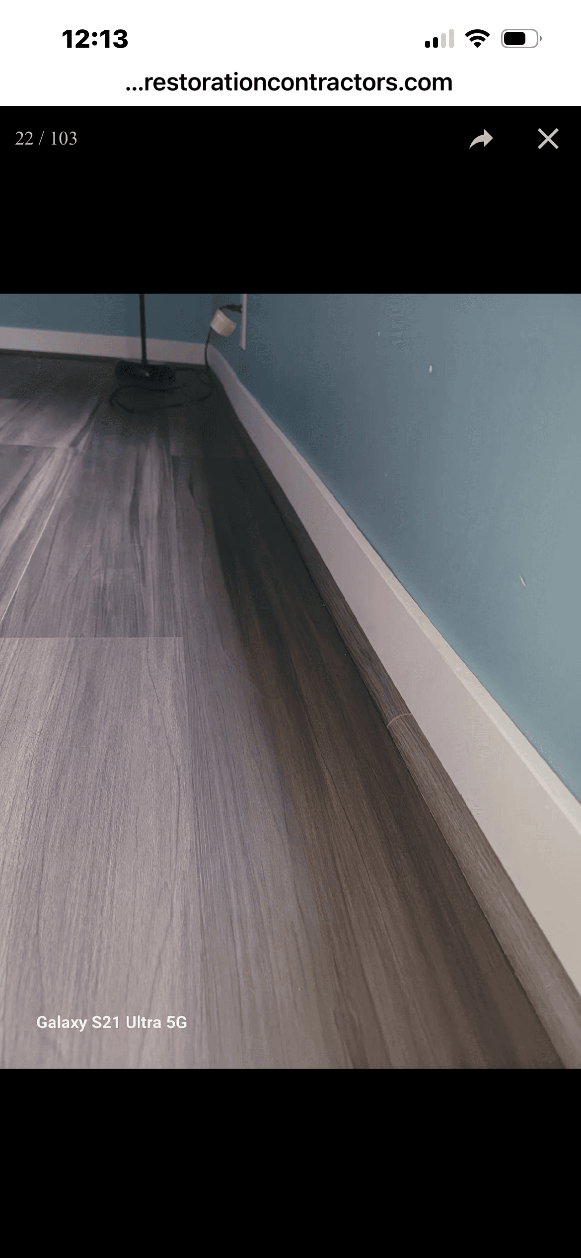 Dark grey wood-look laminate flooring installed against a white baseboard and light blue wall.