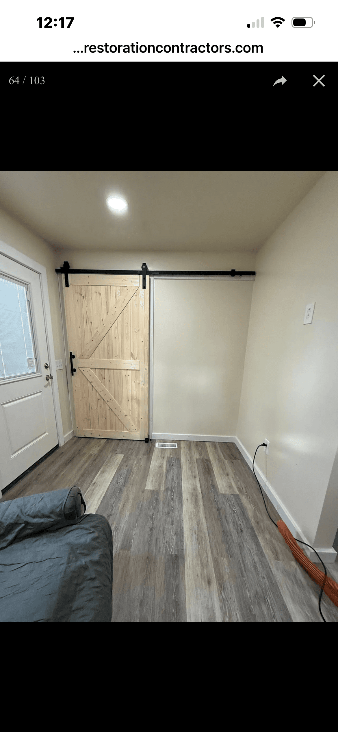 Interior room featuring a light wood sliding barn door, beige walls, and grey wood-look flooring.