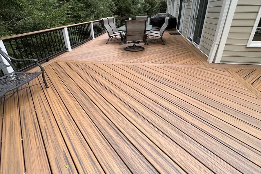Spacious brown composite deck featuring diagonal planking, a dining set, and black metal railings.