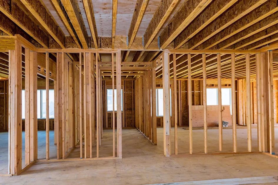Interior framing of a new house showing wooden wall studs, ceiling joists, and subflooring.
