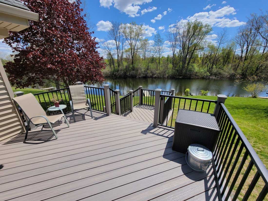 Grey deck with chairs overlooking a calm river and green trees under blue skies.